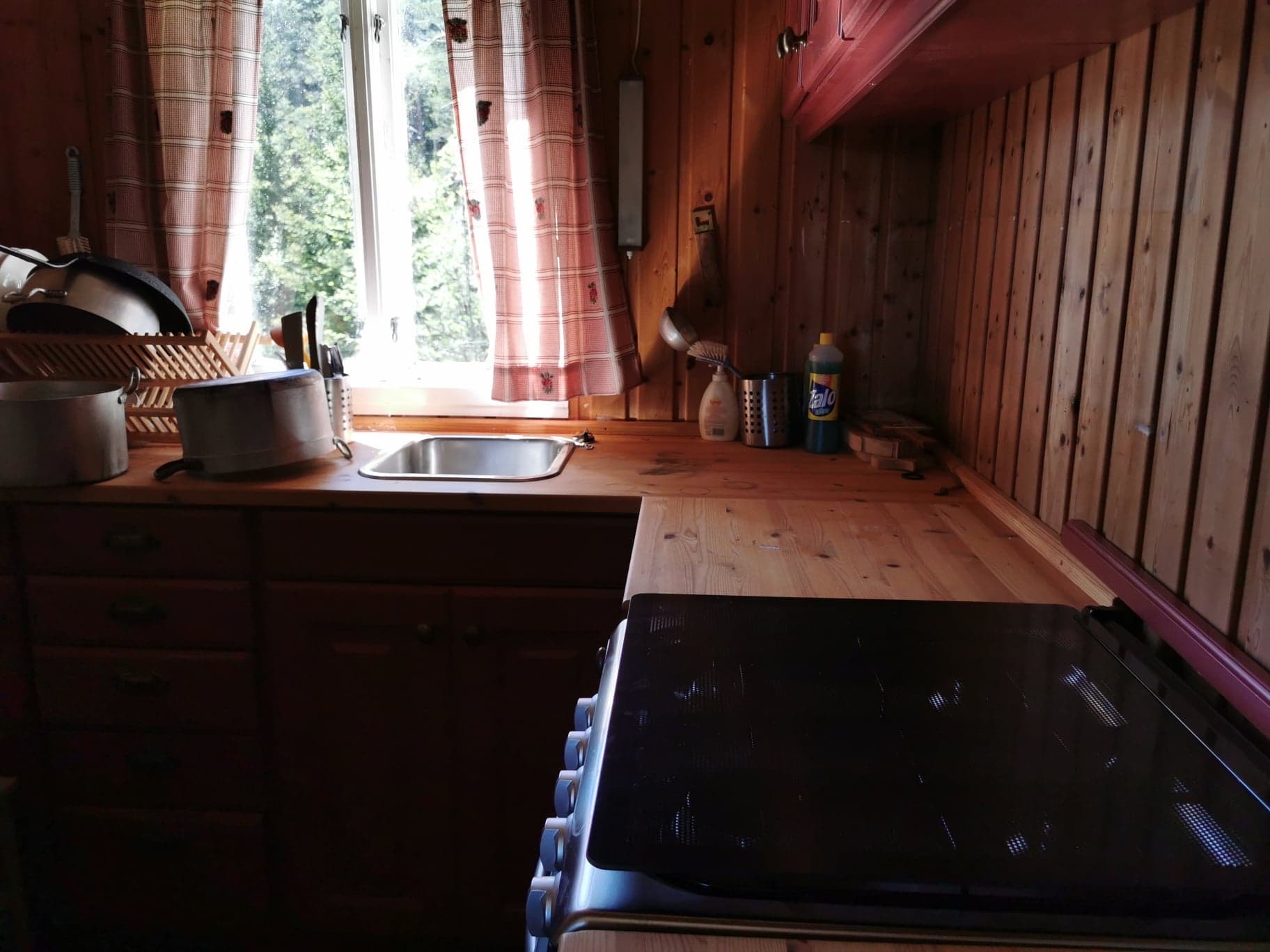 Kjøkkenbenk med vask, oppvaskstativ og vindauge som slepper inn lys i hytta