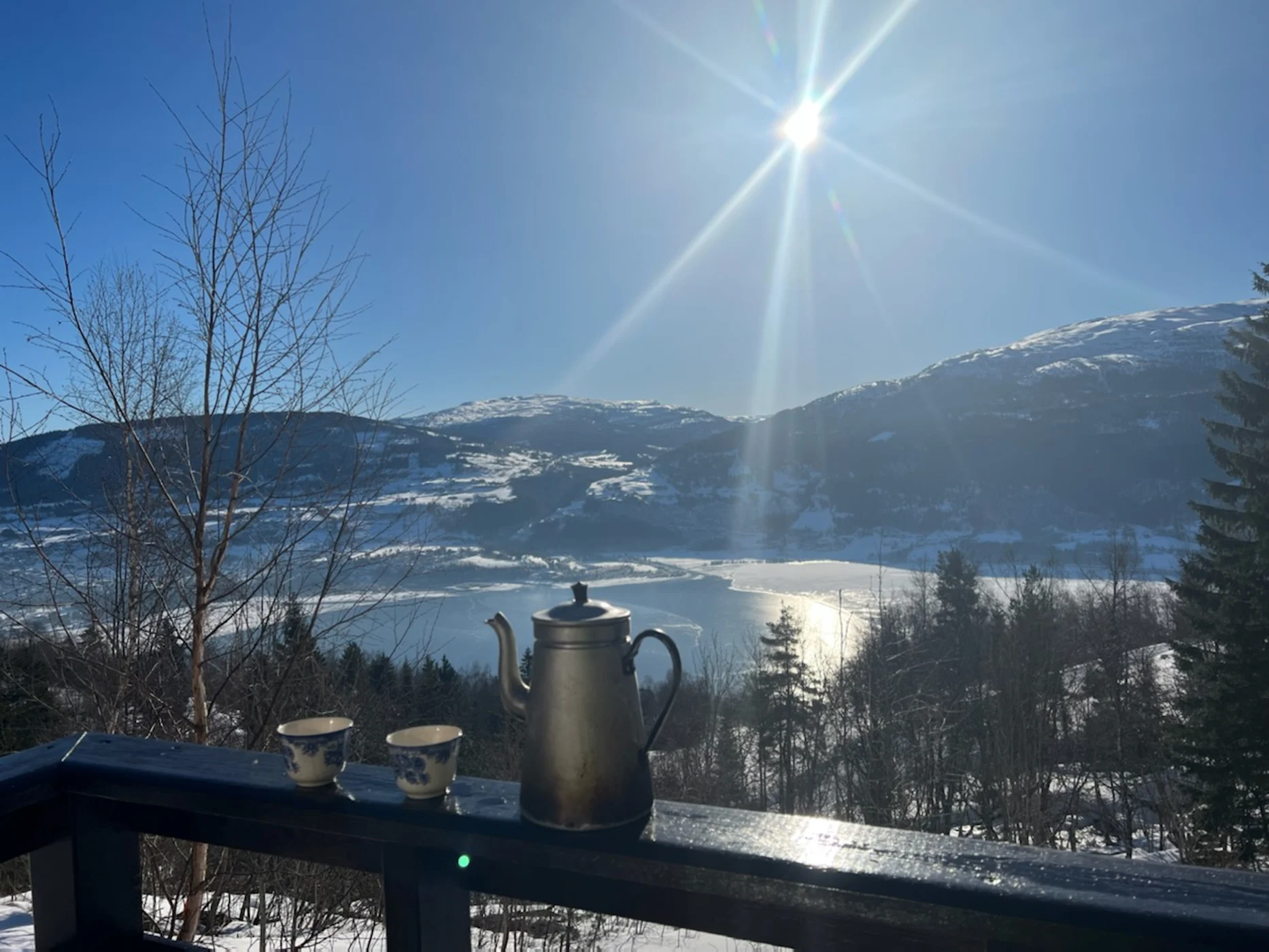 Varm kaffikopp på hytteverandaen med snødekte fjell i bakgrunnen