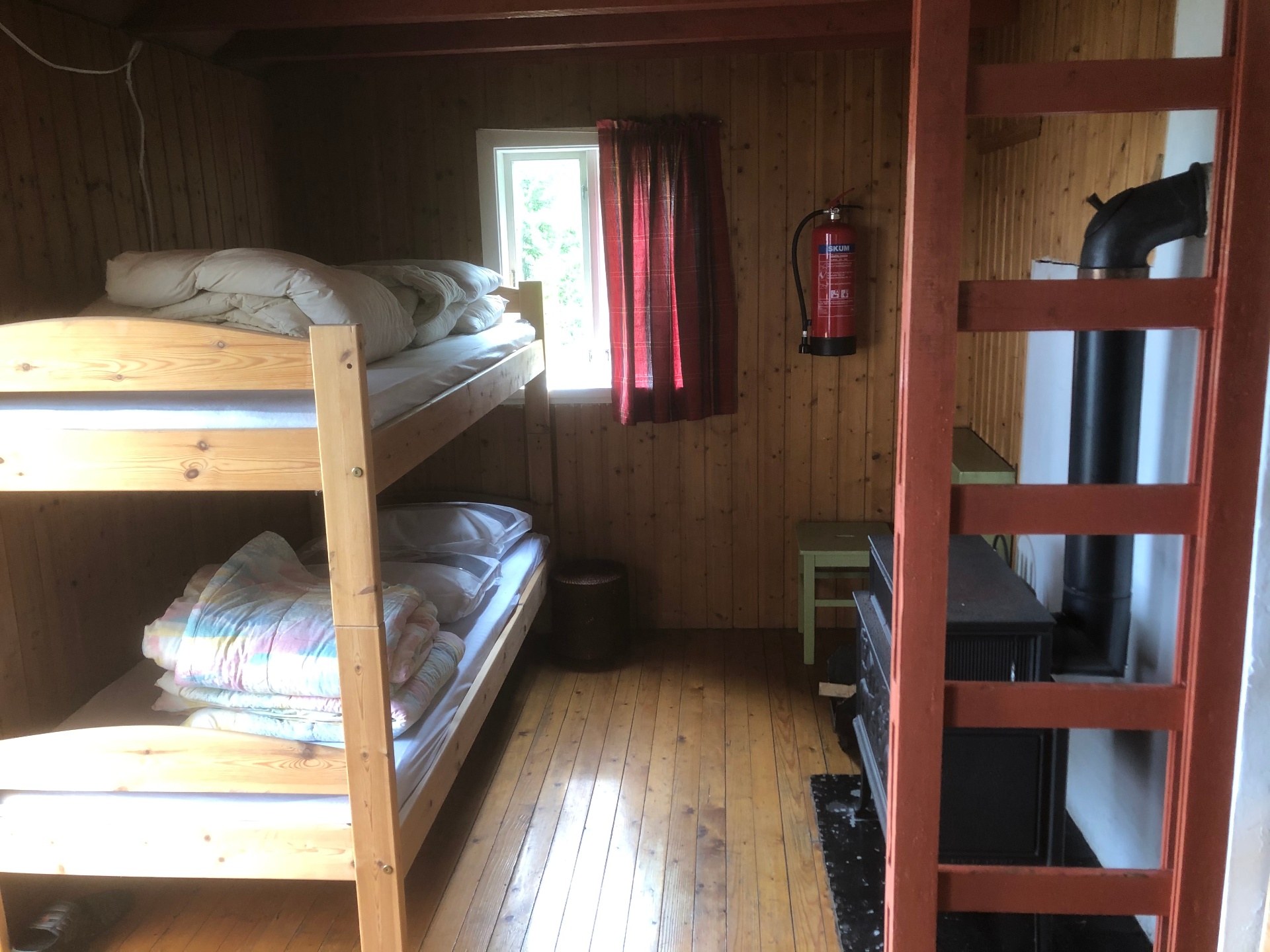 Køyesenger i soverommet med raude gardiner og vedovn